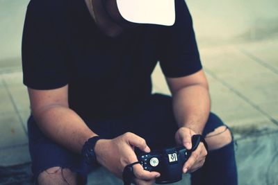 High angle view of man holding camera while sitting on footpath