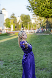 Beautiful blonde with long hair and long purple dress is balancing in public park. 