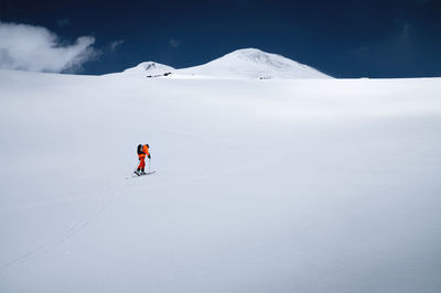 A young sportsman skier in an orange suit climbs a ski tour on a snow-covered slope to mount elbrus.