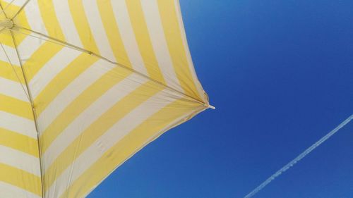 Cropped image of striped beach umbrella against blue sky with vapor trail