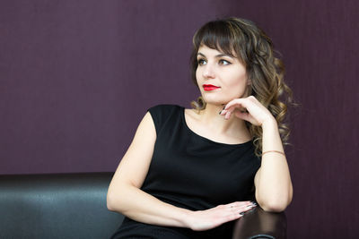 Portrait of a young woman sitting against wall