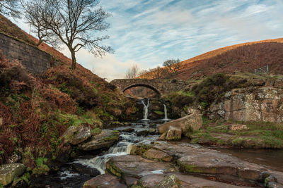 Arch bridge over stream against sky