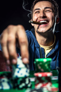 Smiling man playing poker with cigar against black background