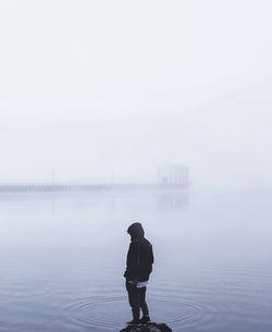 Rear view of person standing in lake during foggy weather