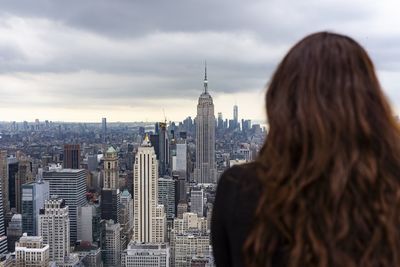 Rear view of woman looking at city buildings against cloudy sky