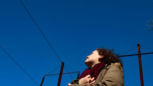 Low angle view of girl looking away against blue sky