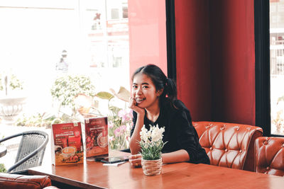 Portrait of young woman sitting on table at restaurant