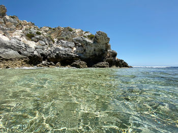 Rock formation in sea against clear blue sky