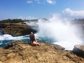 Woman sitting on rock against sky