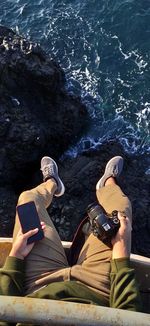 Directly above view of man holding camera and smart phone over against seashore