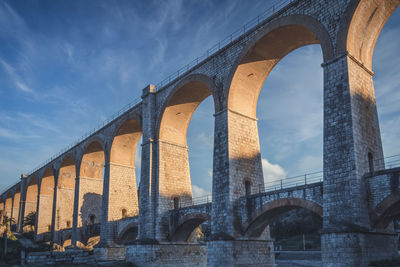 Low angle view of bridge over river against cloudy sky