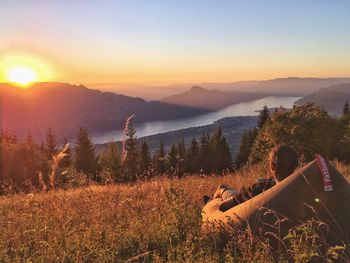 Rear view of man relaxing on bean bag at mountain peak looking at sunset over lake