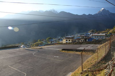 Road by buildings and mountains against sky