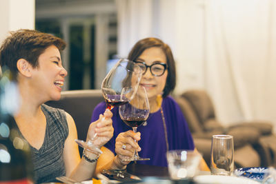 Happy family daughter toasting glasses of red wine with mother at home.