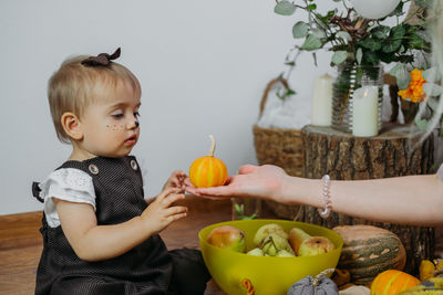 Cute baby girl holding fruits while sitting at home
