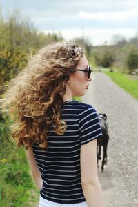 Rear view of young woman standing on footpath against cloudy sky