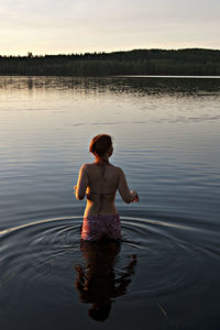 Rear view of woman standing amidst lake during sunset