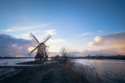 Traditional windmill on shore against sky during sunset