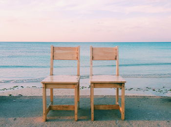 Empty wooden chairs at beach against sky