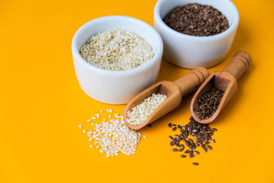 Wooden spoons with sesame and flax seeds lies in a white mortar on a yellow background. healthy eat