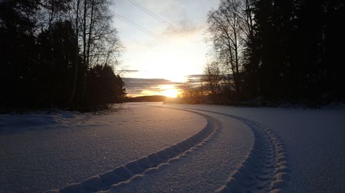 Snow covered road against sky during sunset