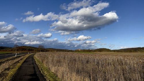 Empty road amidst field against sky