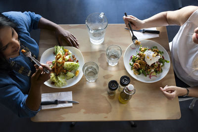 High angle view of friends talking while eating food on table in cafeteria