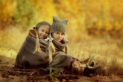 Lovely sisters are sitting, wrapped in a warm blanket, in an autumn park among the golden trees