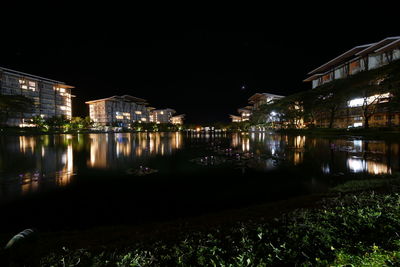 Illuminated buildings by river against sky at night