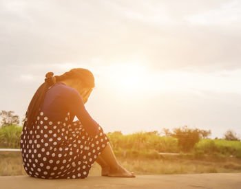 Rear view of woman sitting on land against sky