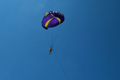 Low angle view of people paragliding against clear blue sky