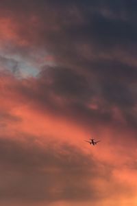 Low angle view of airplane flying in cloudy sky during sunset