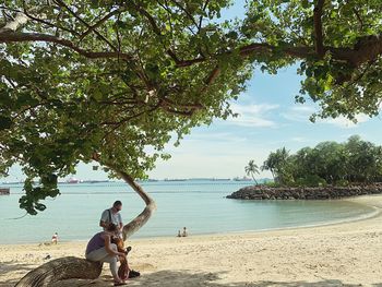 People sitting on beach by sea against sky