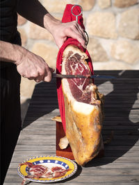 Man cutting a slice of dried spanish jamon serrano on wood table.