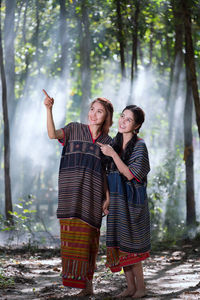 Smiling friends looking up while standing by tree in forest