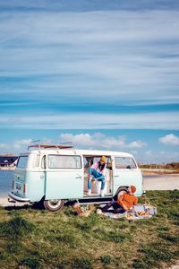 People sitting on land by sea against sky