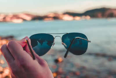 Cropped hand holding sunglasses against sea during sunset