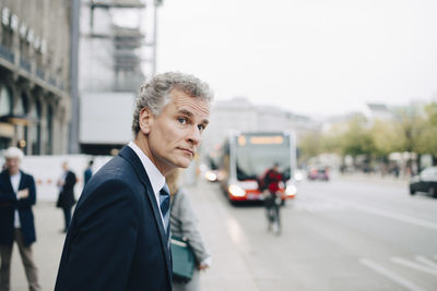 Mature businessman looking away while standing in city