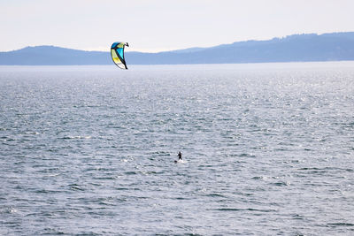 Person paragliding over sea against sky
