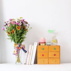 Flowers in vase by books and drawers on table