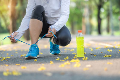 Low section of woman tying shoelace while crouching on road