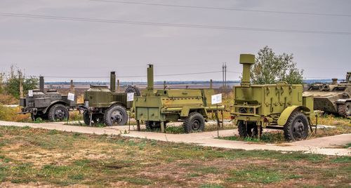 Vehicles on field by road against sky