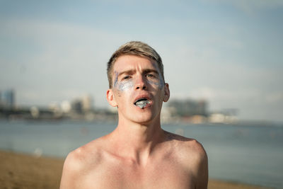 Portrait of young man with glitter in mouth against sea