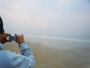Cropped image of person photographing through camera at beach during sunset