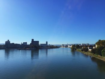 Buildings by river against clear blue sky