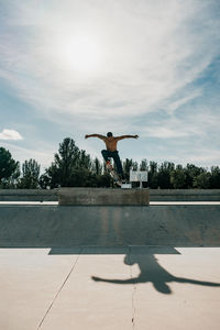 Full length of shirtless man jumping with skateboard outdoors