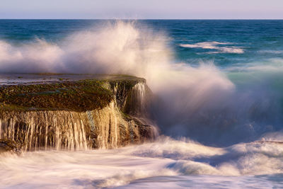 Sea waves splashing on shore against sky