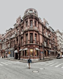 Man walking on road amidst buildings against clear sky