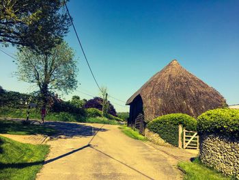 Road amidst trees and houses against clear blue sky