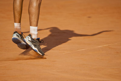 Low section of tennis player playing on field during sunny day